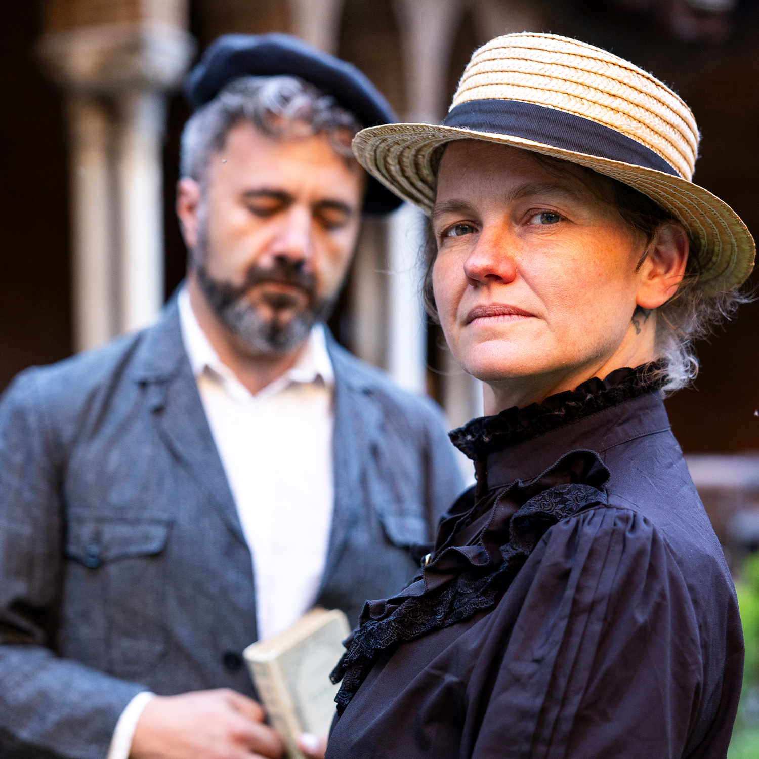 personnage en costume des années 60 avec une femme au premier plan et un homme avec un béret en arrière plan flouté